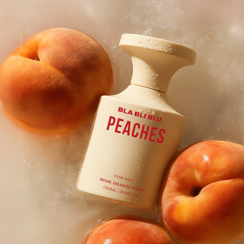 Bottle of BLA BLU PEACHES perfume surrounded by peaches on a textured surface